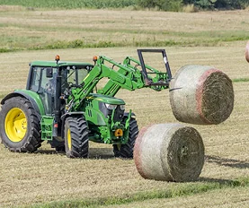Tractor lifting hay bales in field